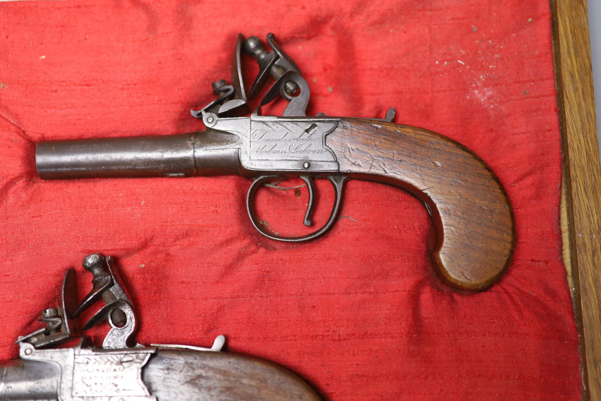Two 19th century Dunderdale, Mabson & Labron steel flintlock pocket pistols, turn off barrels and walnut butts, in a later oak case